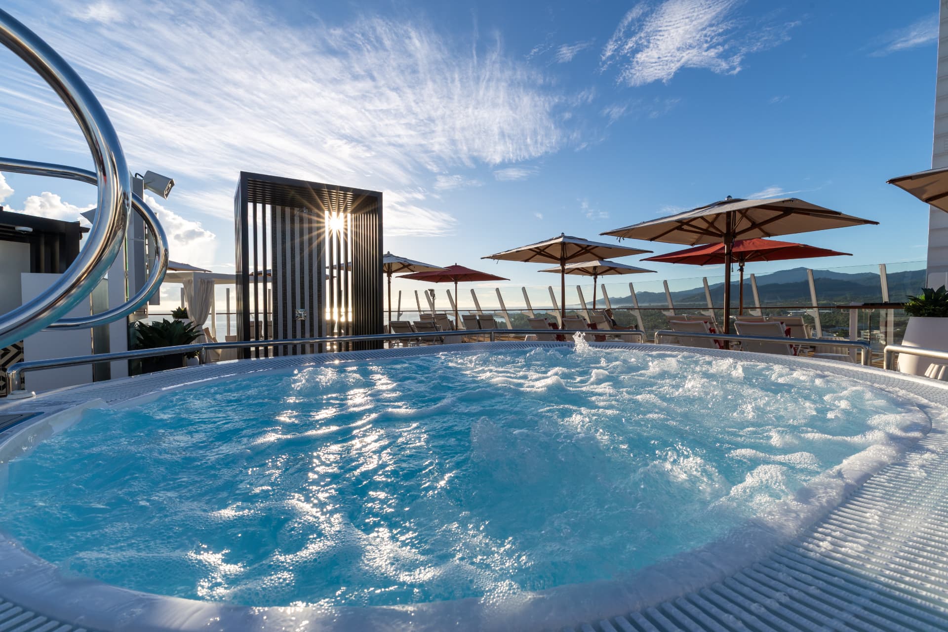 A sunlit outdoor whirlpool and lounge deck aboard a cruise ship.