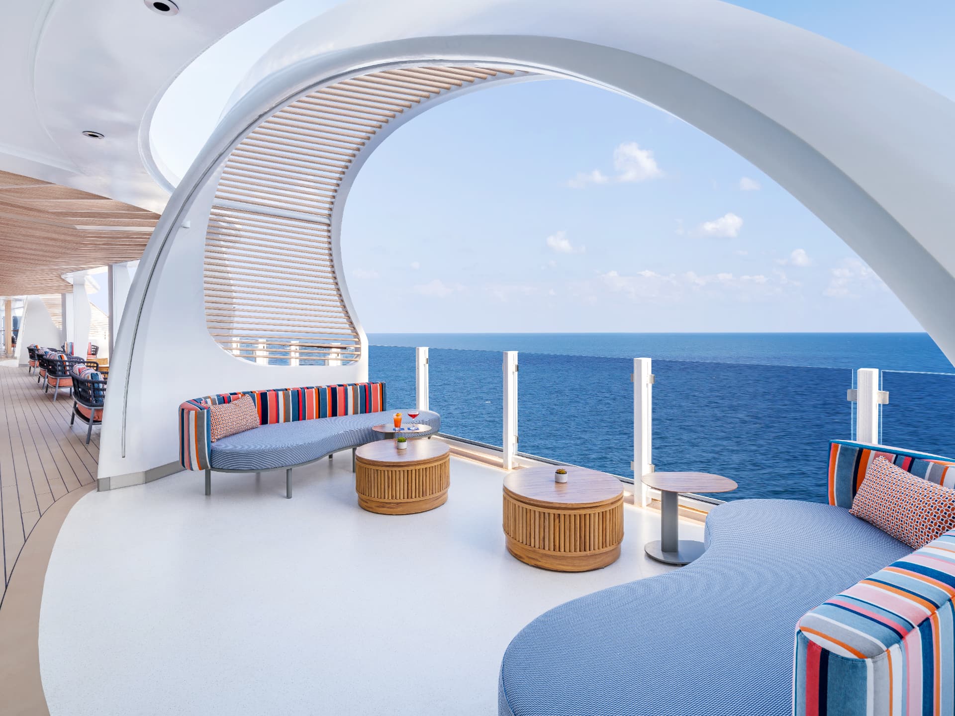 An open-air ship lounge with curved sofas and wide ocean views along the waterfront promenade.