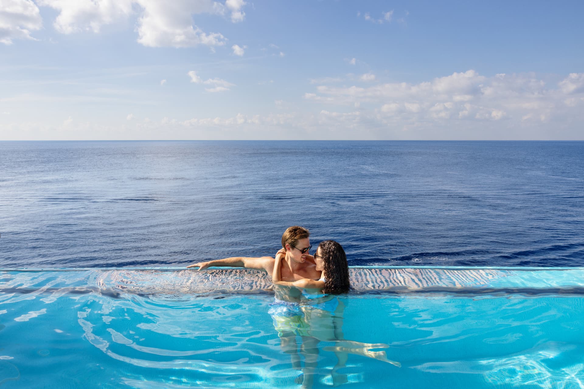 A couple relaxing at the edge of a ship's infinity pool overlooking the open ocean