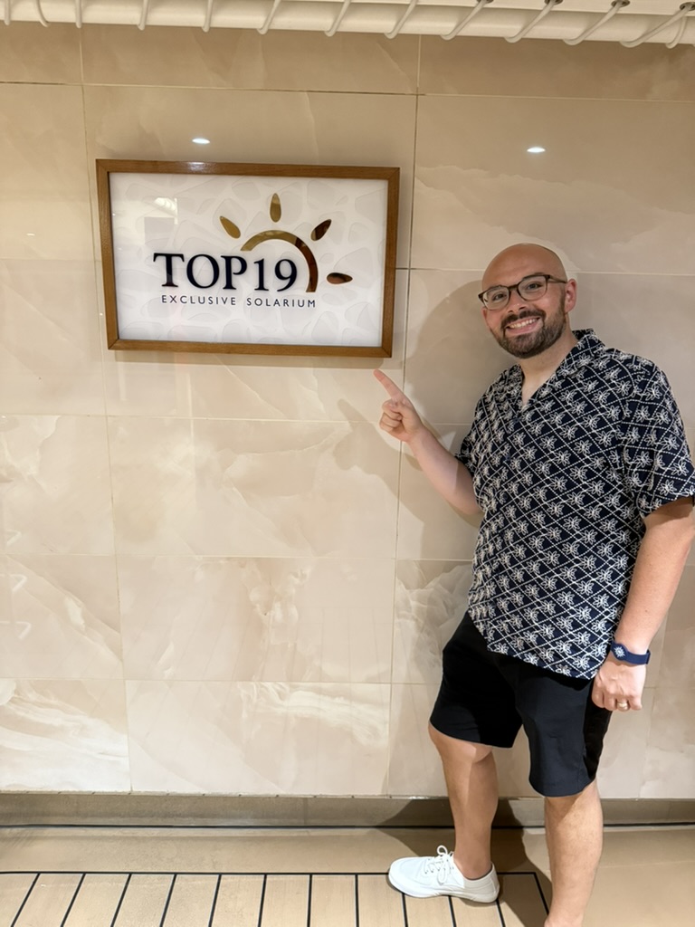 Chris pointing to the Top 19 Exclusive Solarium sign aboard an MSC ship.
