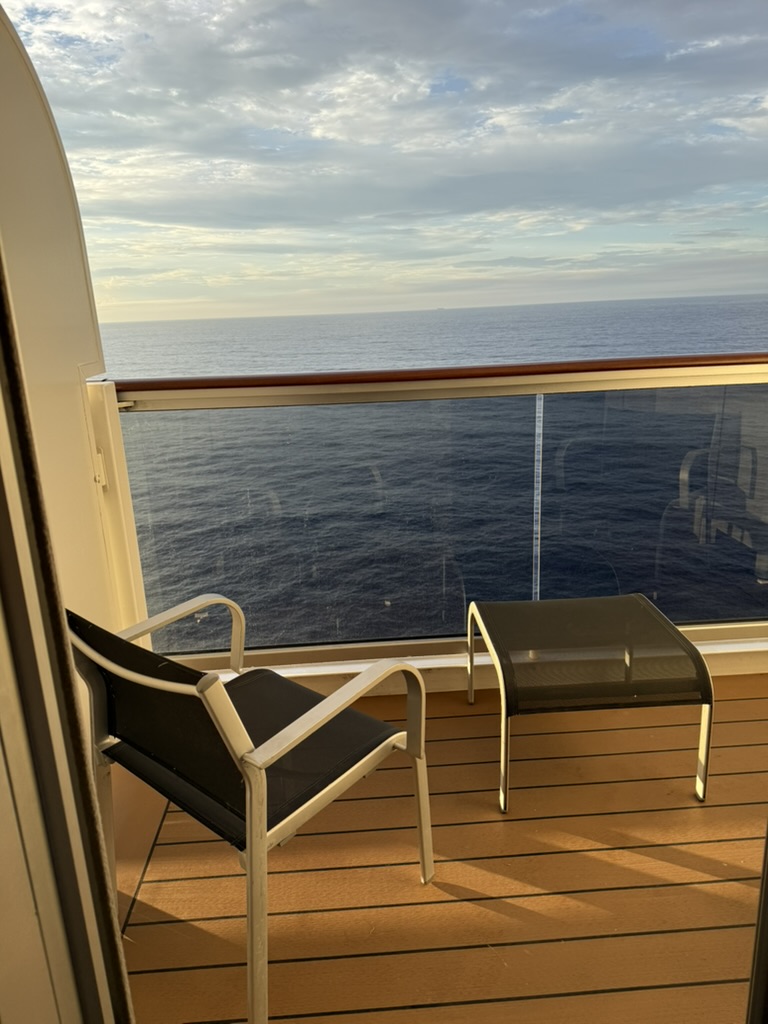 A private balcony with a chair and footstool looking out over open ocean at sunrise.