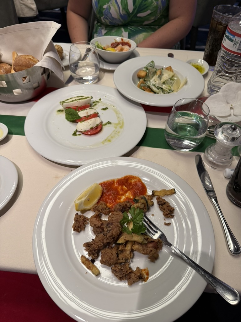 A table set with fried calamari, caprese salad, Caesar salad, bread, and water glasses in an MSC dining room.