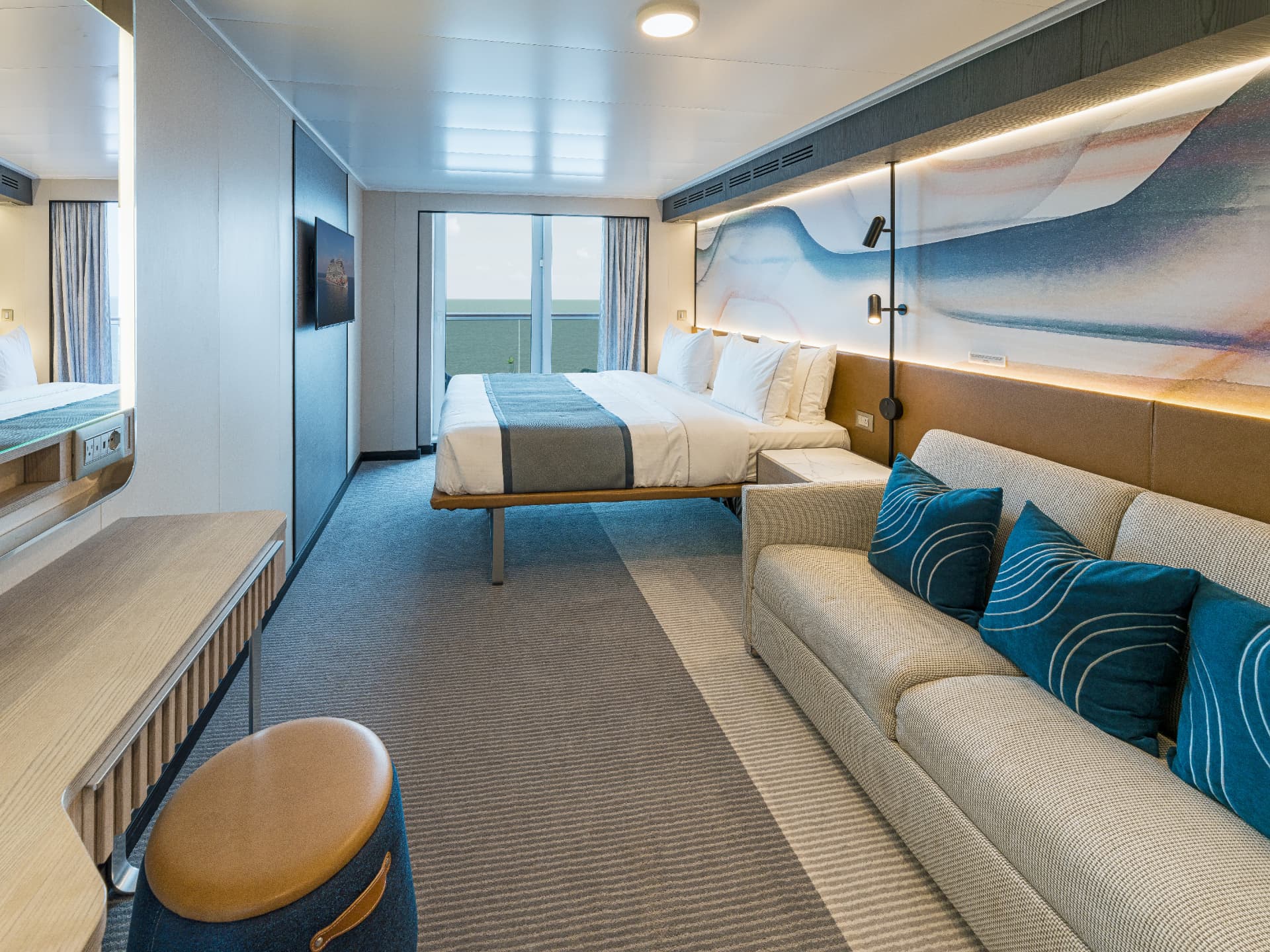 A Norwegian stateroom with a large bed, sofa seating, and a balcony door looking out to the sea