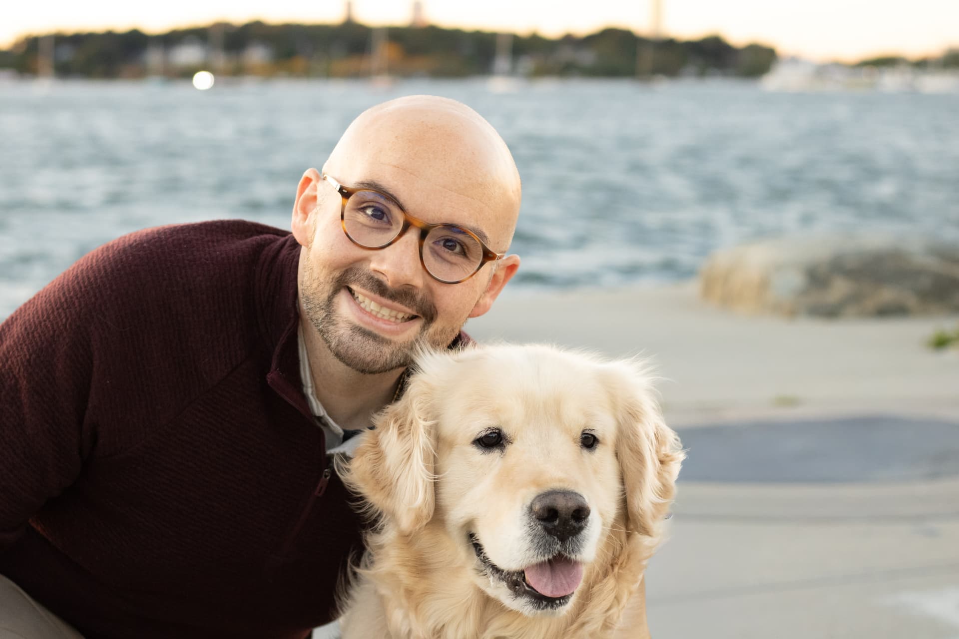Chris of Golden Hour Travel smiling beside his golden retriever, Colby, on the waterfront.