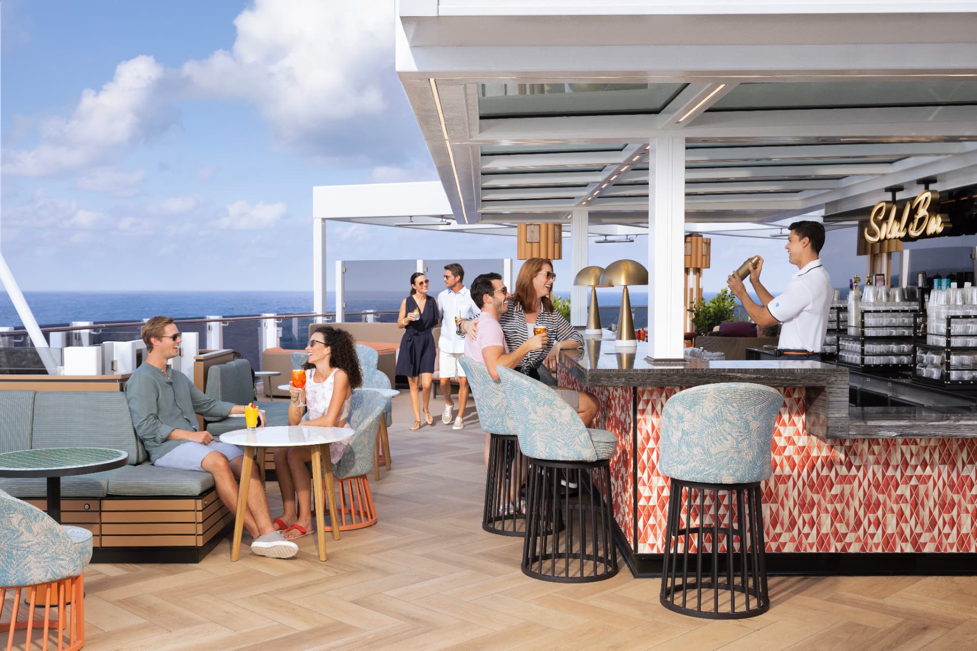 Guests enjoying drinks and conversation at a sunny outdoor bar and dining deck