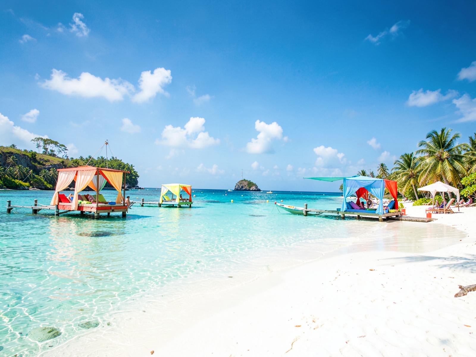 Bright private island beach with clear turquoise water and colorful cabanas