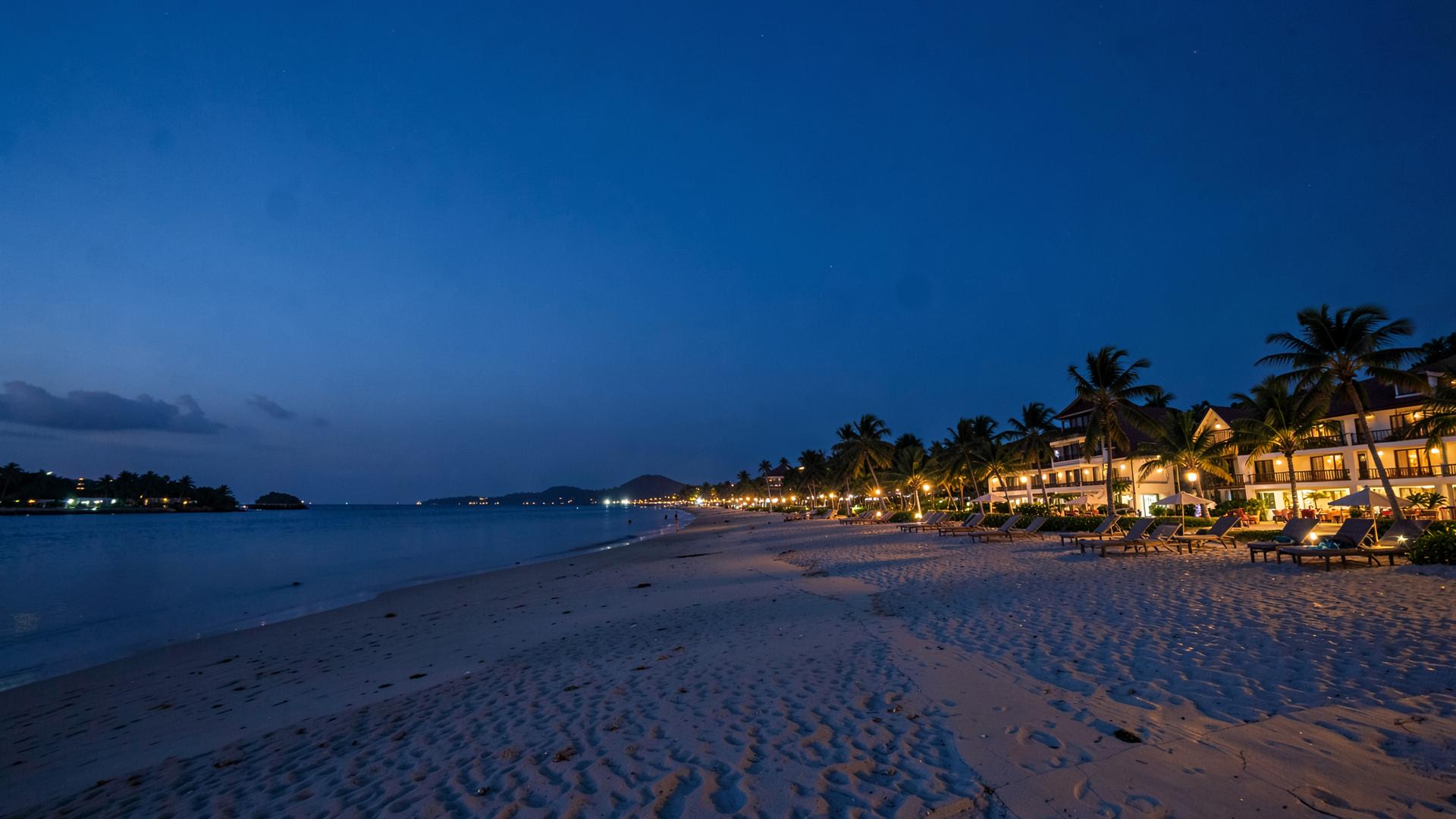 A beachfront resort glowing with warm light at twilight.